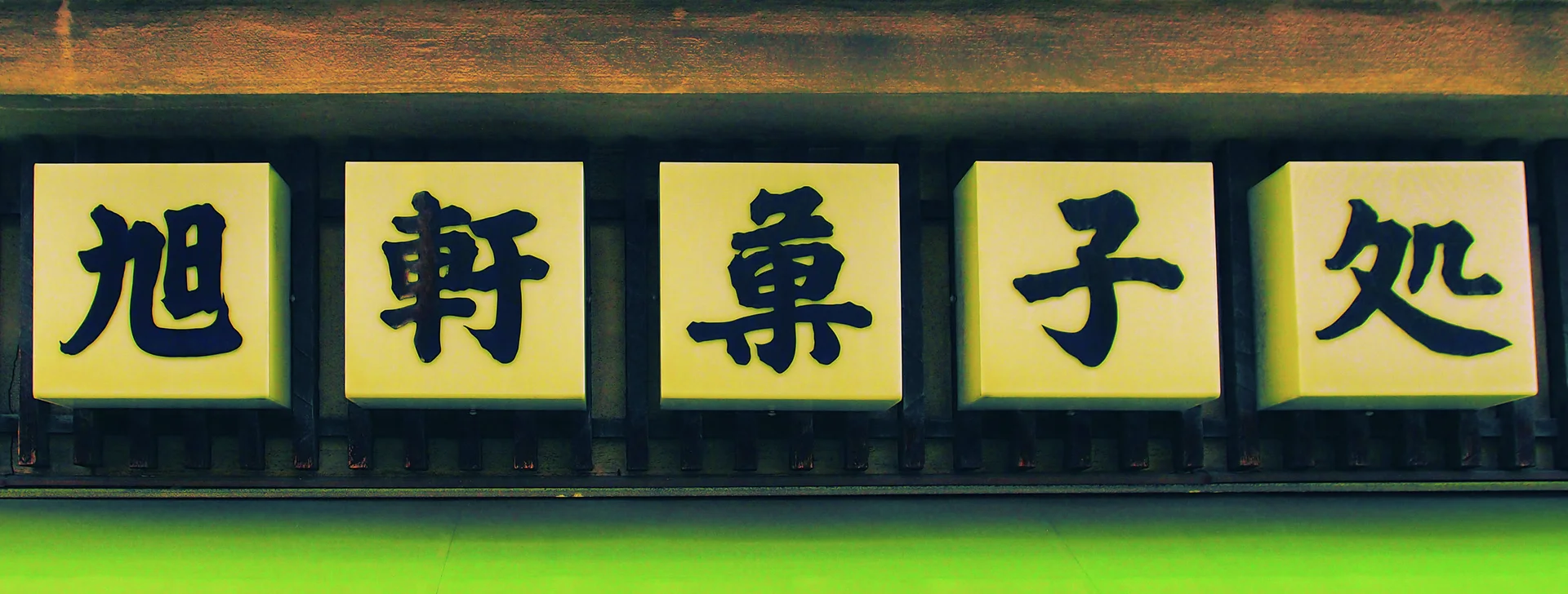 Five yellow square panels display bold dark characters in a row beneath a wooden beam.