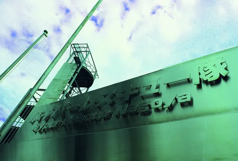 Raised lettering decorates a green-toned industrial facade beneath ladders, poles, and cloudy sky.
