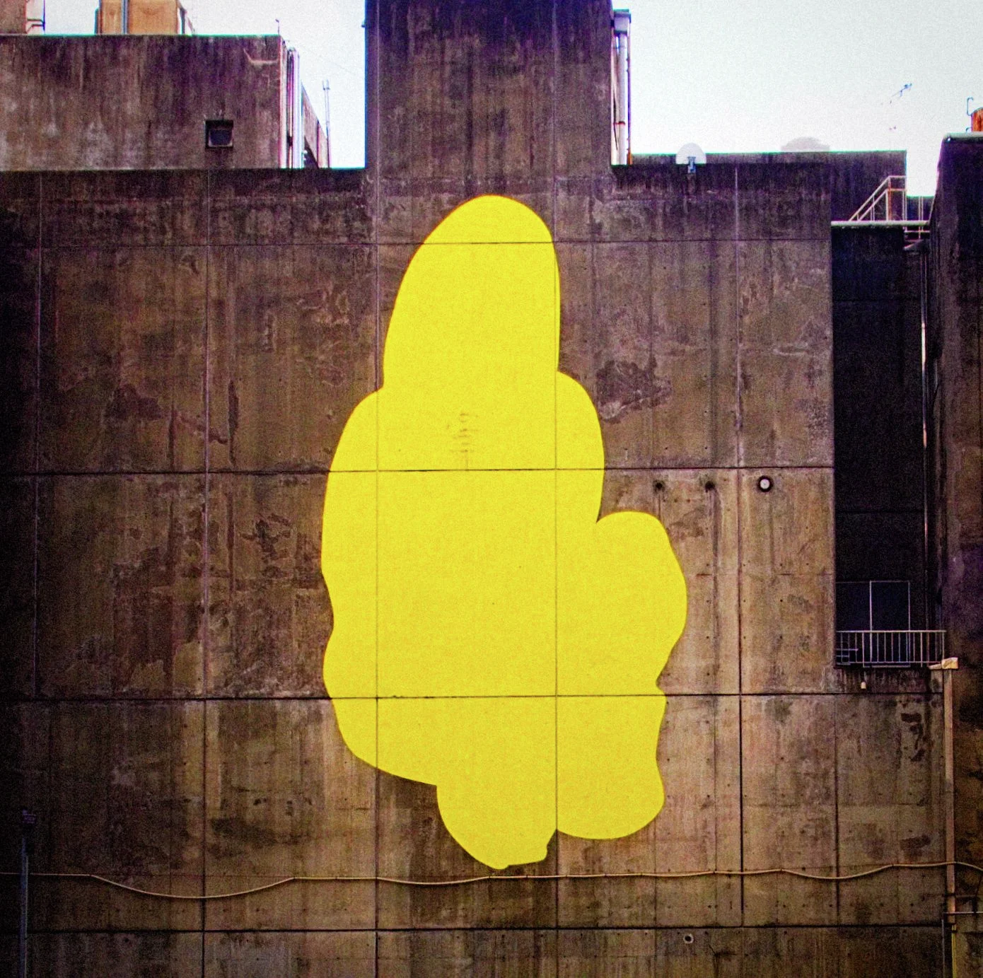 A large irregular bright yellow shape covers a stained concrete wall between dark building openings.