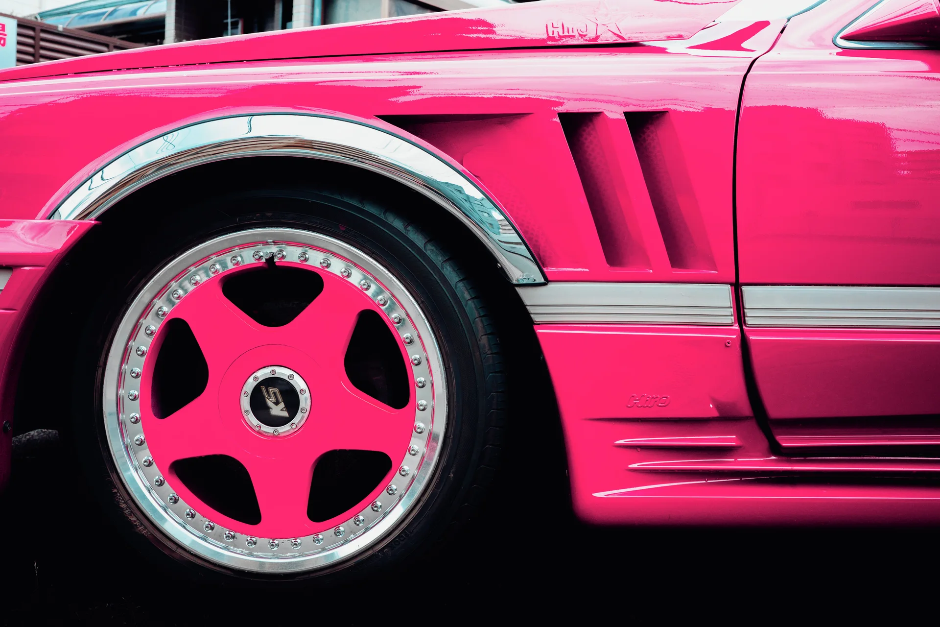 A vivid pink car has a matching wheel center, chrome trim, and sculpted vents along its side.