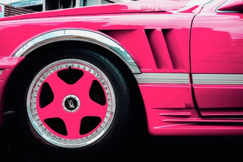 A vivid pink car has a matching wheel center, chrome trim, and sculpted vents along its side.