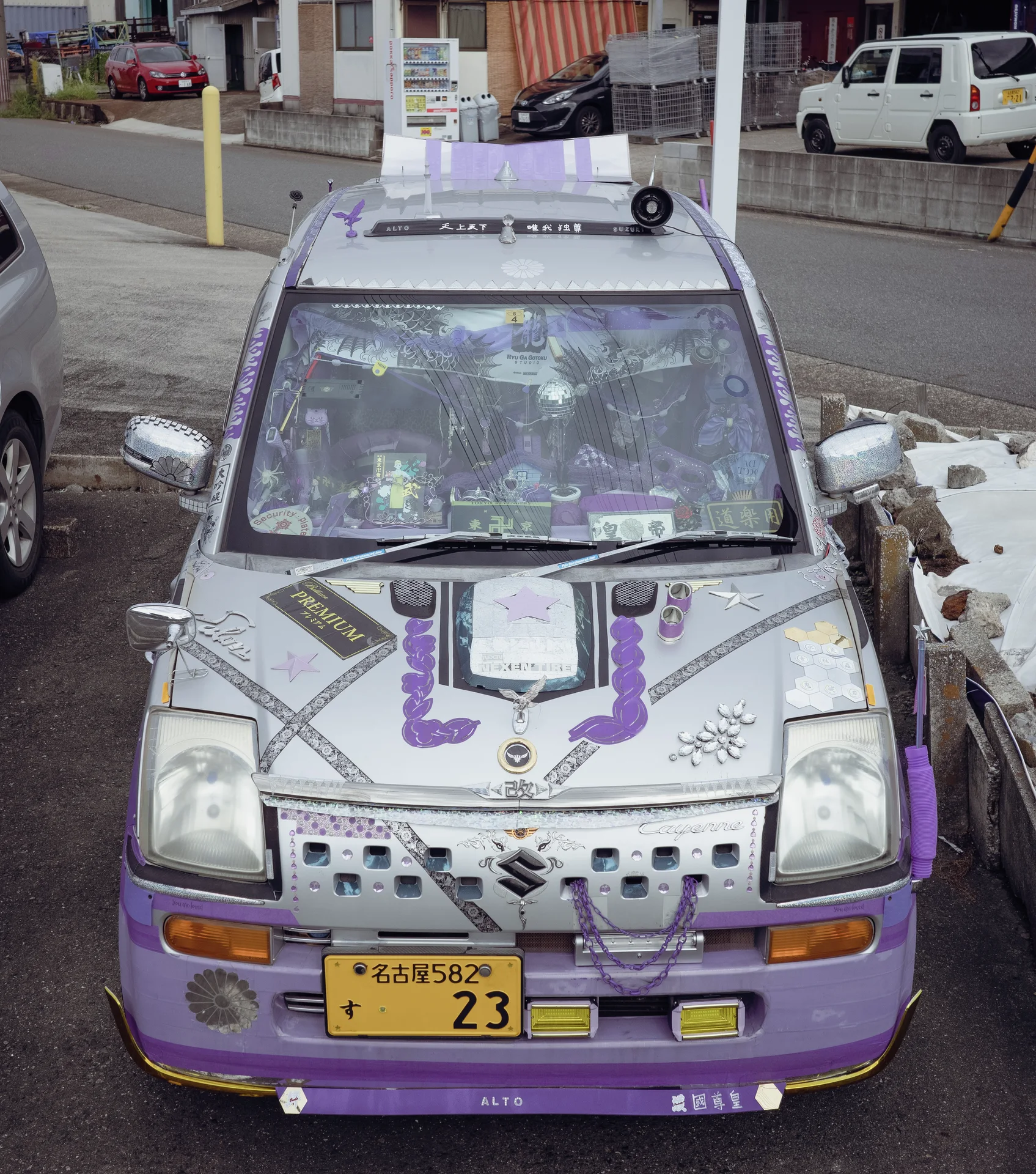 A silver compact vehicle with purple trim and densely decorated windshield sits beside a low stone wall.