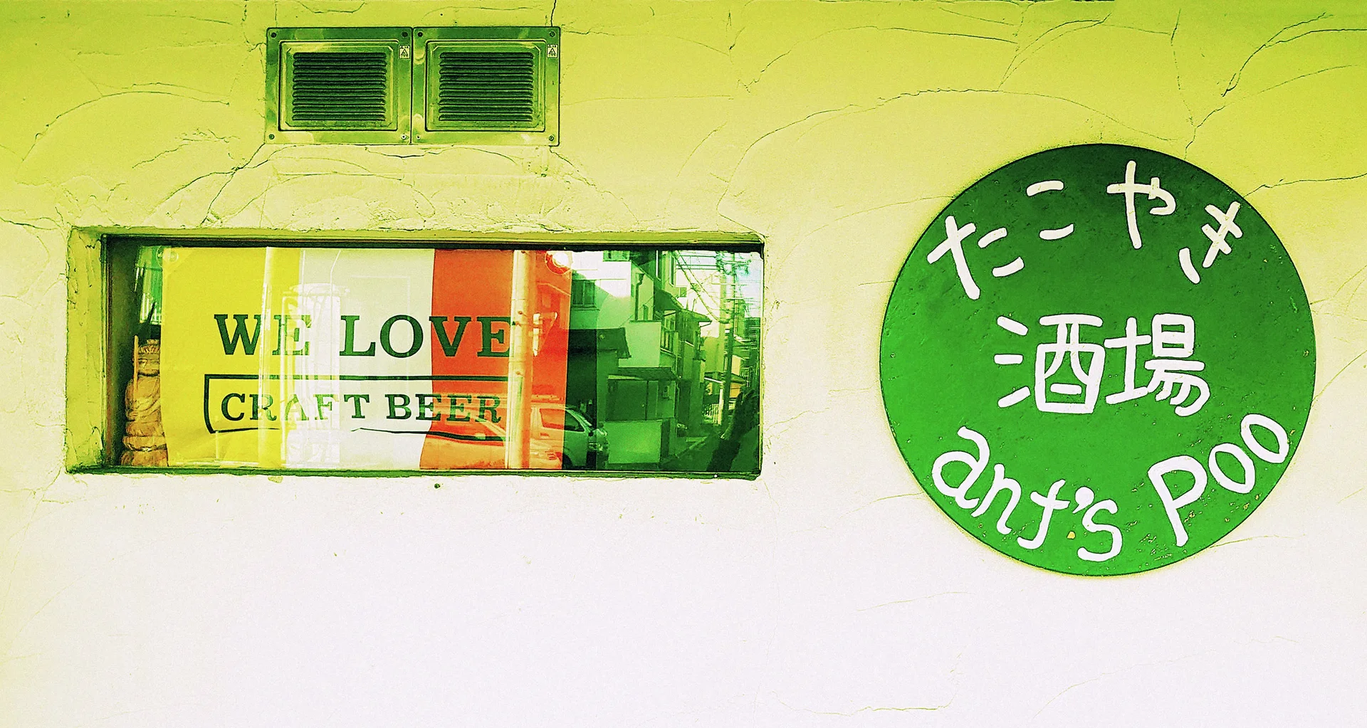 A narrow window with craft beer lettering sits beside a green circular sign on a pale wall.