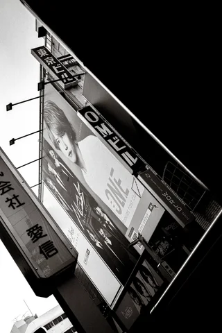 Projecting shop signs overlap above a narrow street, seen at a diagonal angle in black and white.