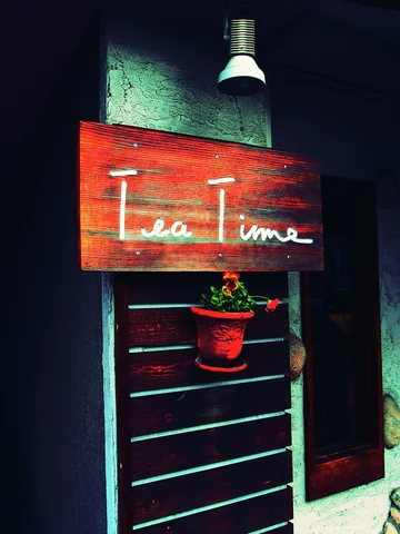 White Tea Time script marks a small red wooden sign above a hanging flower pot beneath a lamp.