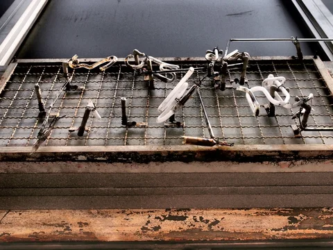 Broken pale lettering and exposed supports cling to a rusted wire-grid sign below a dark window.