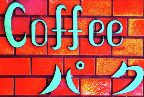 Turquoise raised coffee lettering and Japanese characters contrast with a vivid red brick-patterned wall.