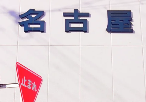 Three large dark Japanese characters project from a pale tiled wall above a red triangular street sign.