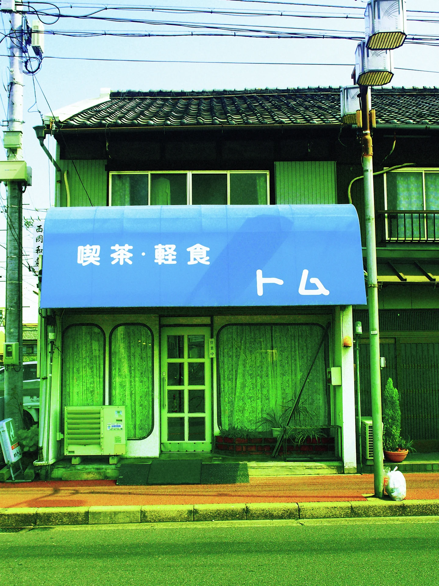A blue cafe awning shades a rounded green doorway beneath a dark tiled roof.