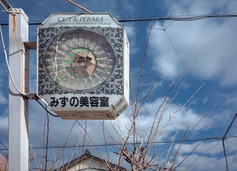 A weathered octagonal sign with a circular patterned center hangs against blue sky and bare branches.