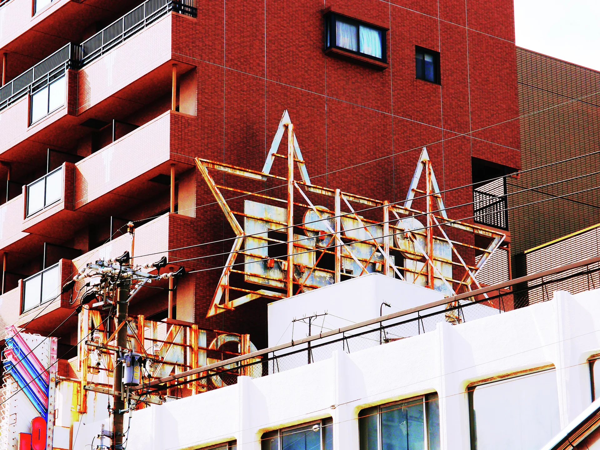 An empty rust-colored rooftop sign frame stands before a red apartment building with stacked pale balconies.