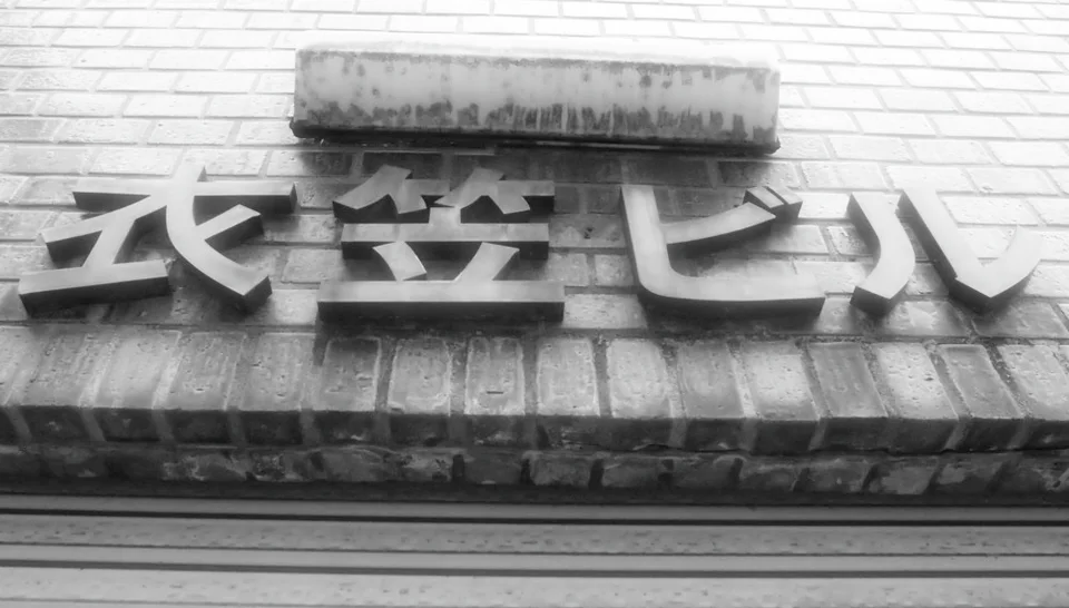 Raised Japanese characters cast dark shadows across a weathered brick-patterned fascia in black and white.