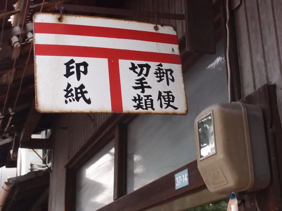 A white sign with red bands and black Japanese lettering hangs beside an old wall-mounted meter.