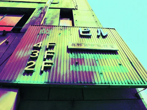 Raised floor numbers and Japanese characters decorate a weathered corrugated canopy beneath tall upper windows.