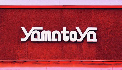 Stylized raised white Yamatoya lettering casts small shadows across a textured red wall.