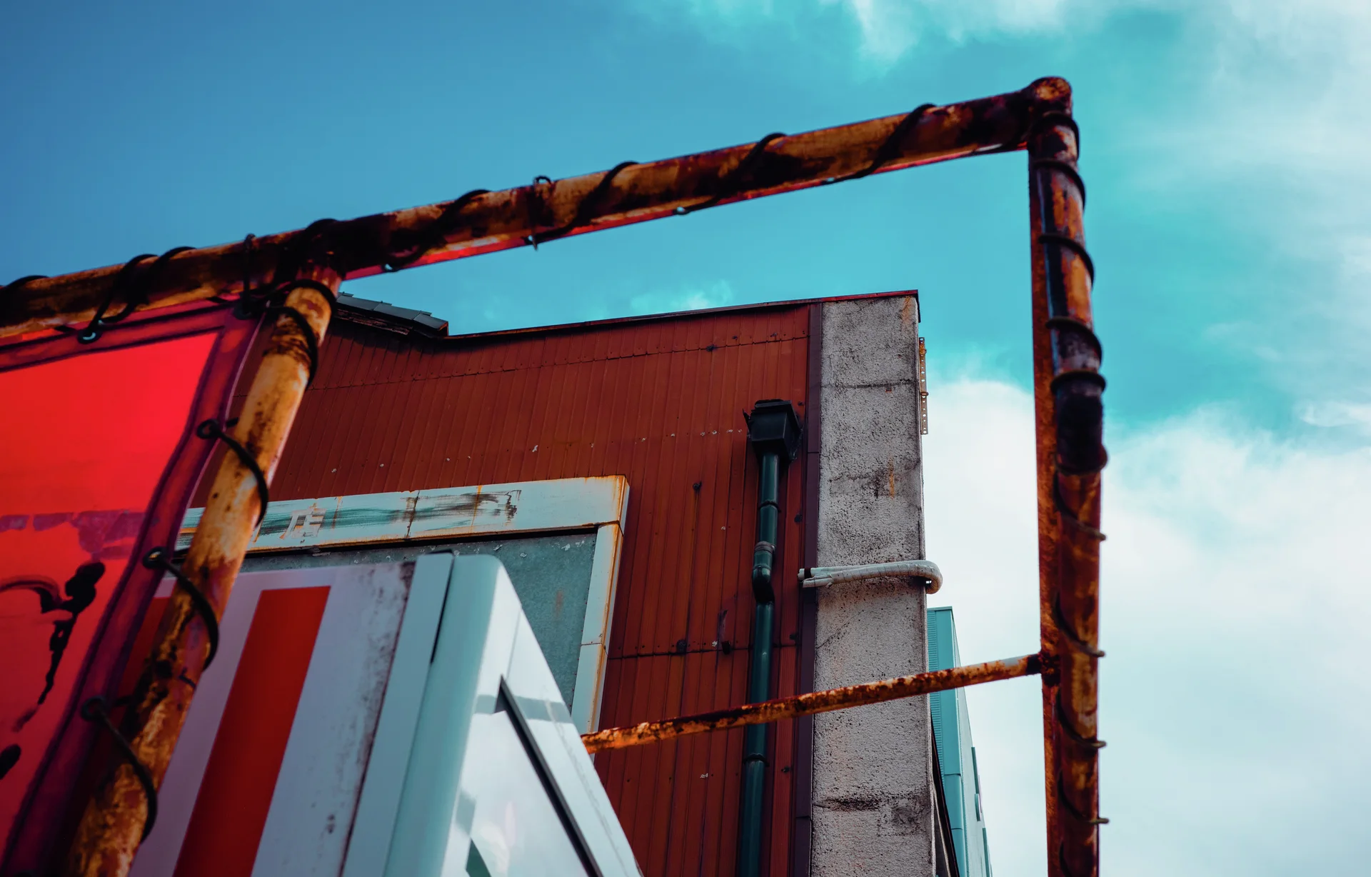Rusted rectangular pipework frames colorful building panels beneath a bright turquoise sky.