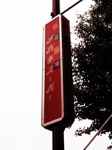 A tall red vertical sign hangs beside silhouetted tree foliage against pale sky.