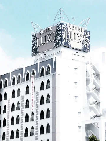 A white building with rows of pointed arched openings rises beneath a large Hotel Luxe rooftop sign.