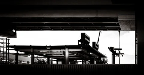 Dark overhead beams frame an open metal structure and utility equipment against a bright sky.