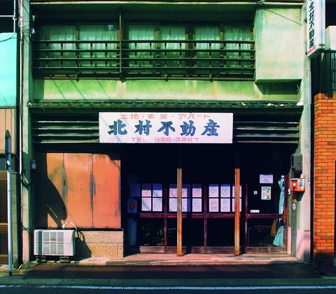 A weathered green storefront has barred upper windows and dark sliding doors beneath a white sign.