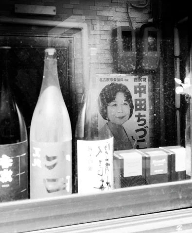 Bottles and boxes sit in a shop window beside a portrait poster in black and white.