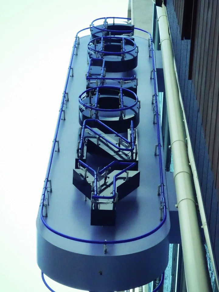 Metal letter frames stand above a long rounded blue-edged projecting sign beside a vertical drainpipe.