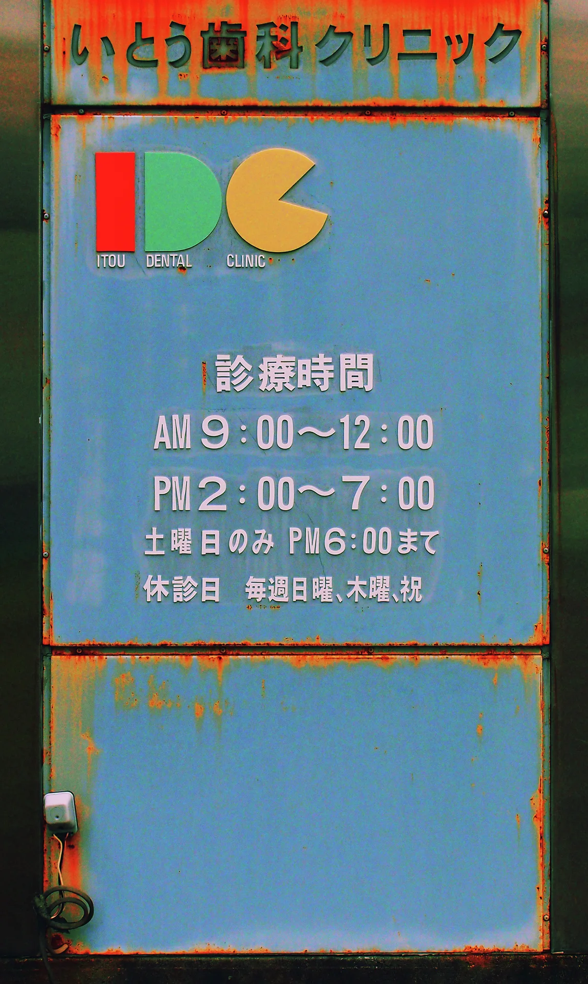 A blue clinic sign displays colorful geometric shapes above white hours and rusted edges.