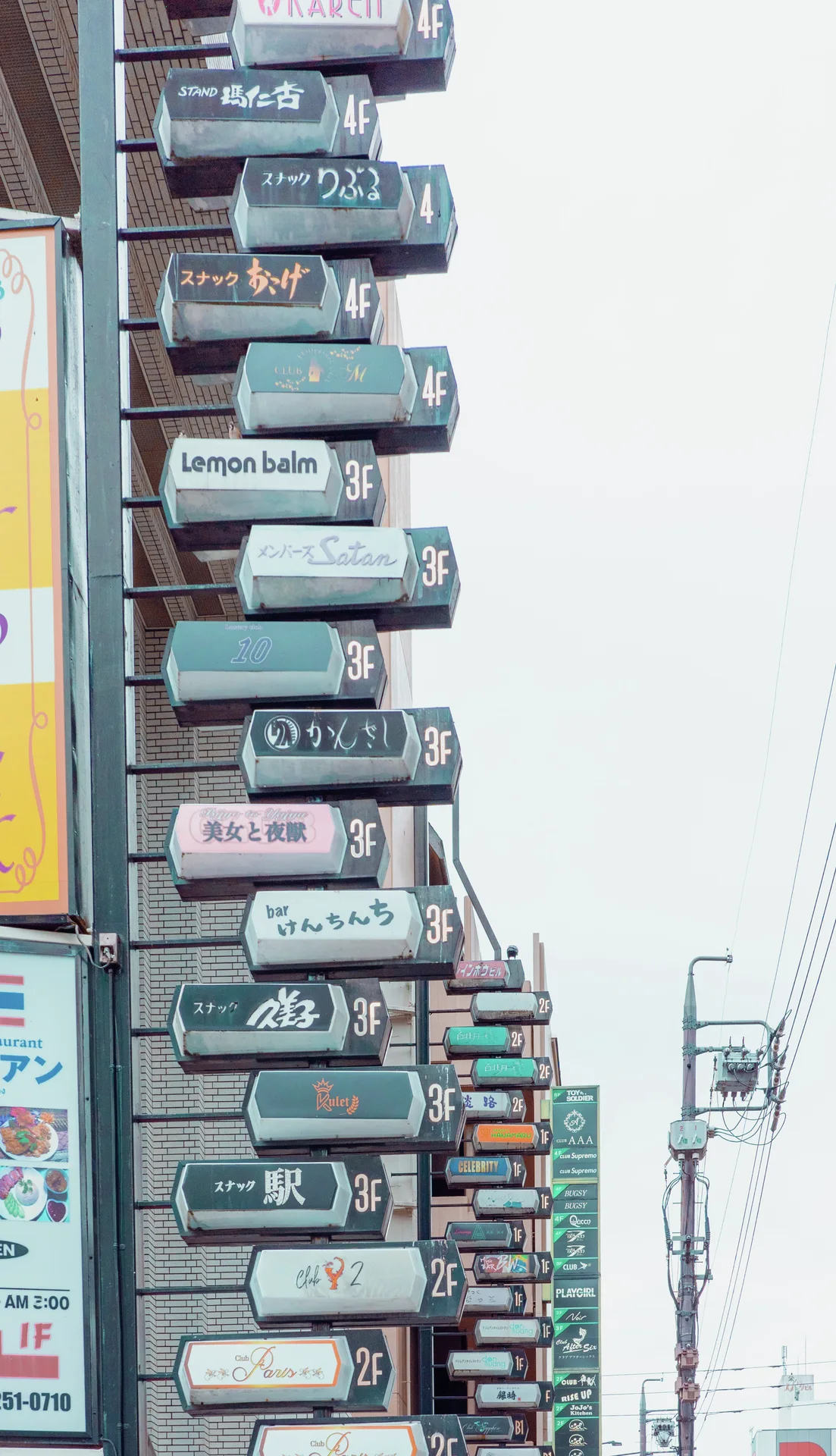 A tall stack of narrow projecting business signs climbs a building facade beside a streetlight.