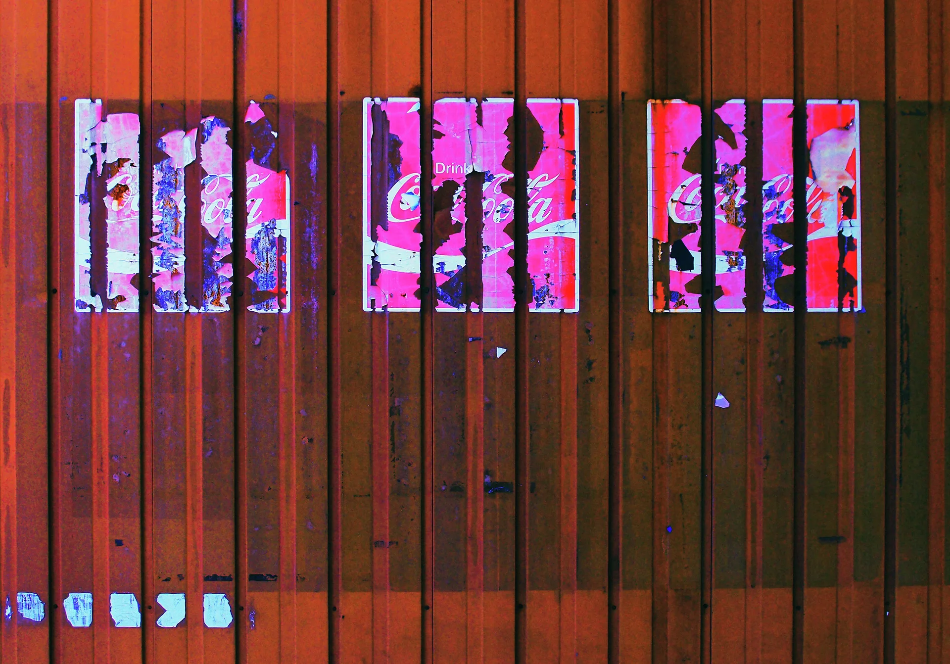 Pink posters show through vertical metal bars across a weathered reddish wooden wall.
