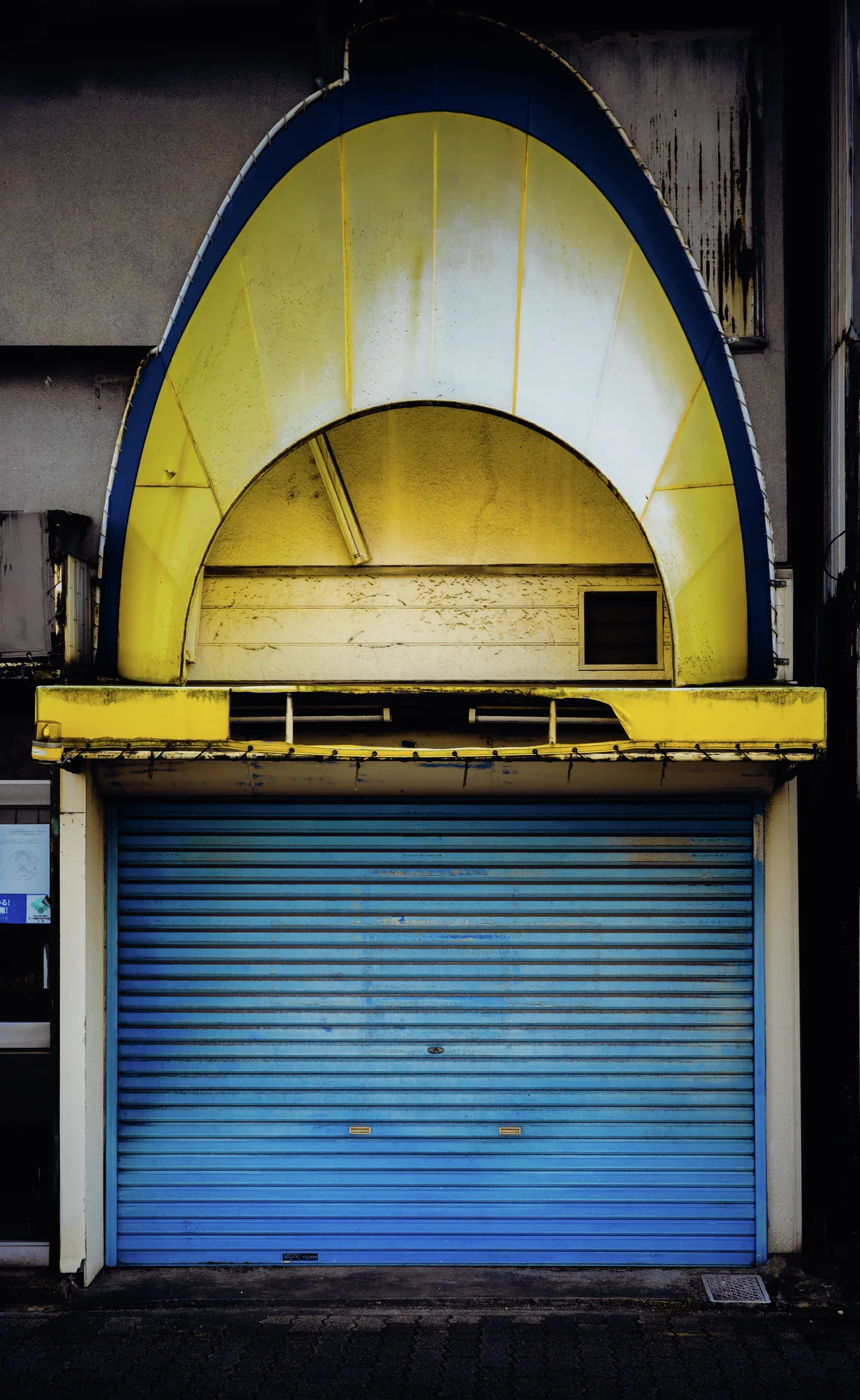 A tall yellow arched panel framed in blue rises above a closed turquoise metal shutter.