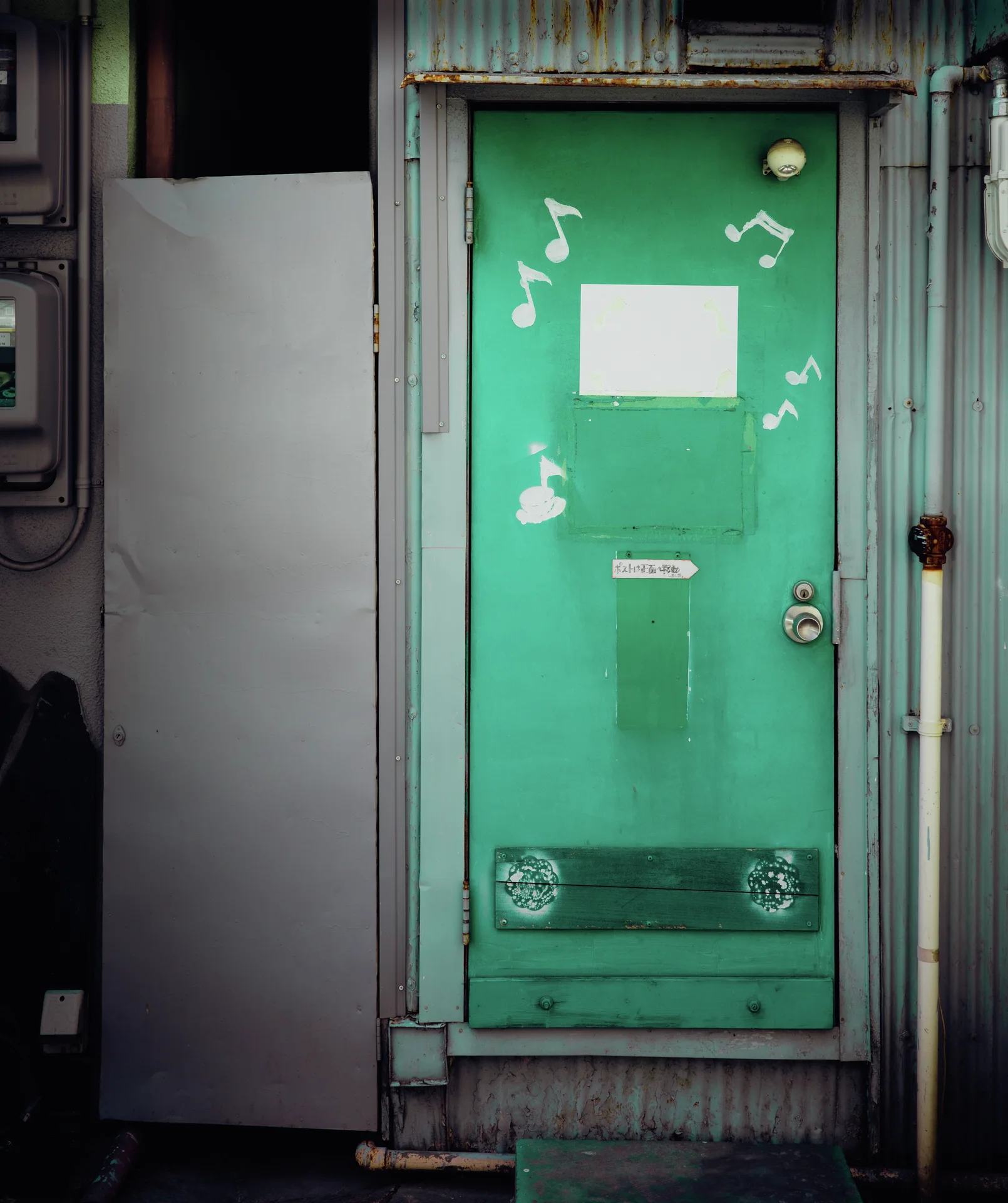White musical notes decorate a narrow green door set within weathered pale corrugated metal siding.
