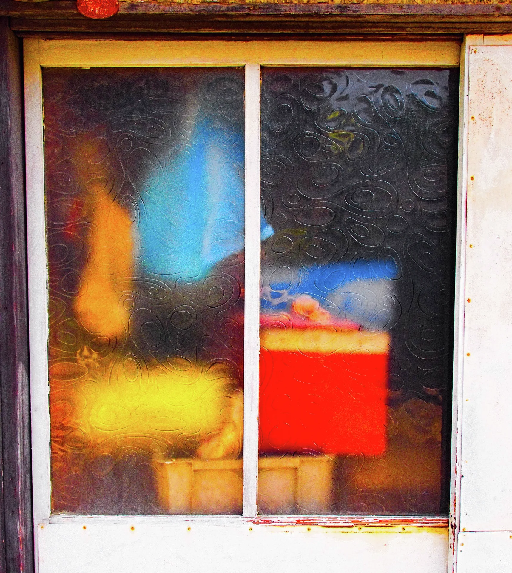 Frosted sliding window panes reveal blurred yellow, blue and red shapes behind a white frame.