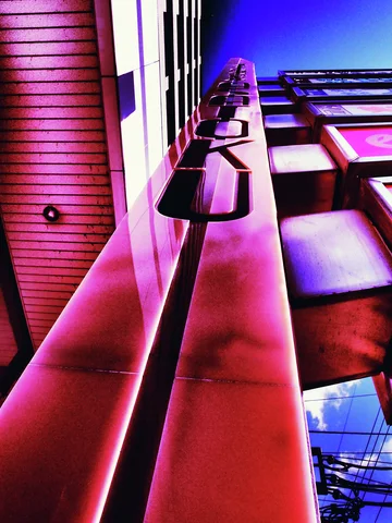 An upward view follows shiny red structural beams and projecting brackets toward a deep blue sky.