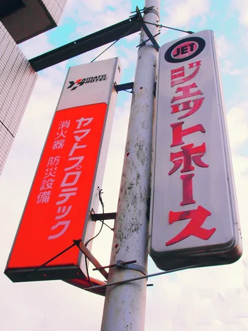 Two tall red-and-white signs project beside a pale concrete utility pole beneath a cloudy sky.