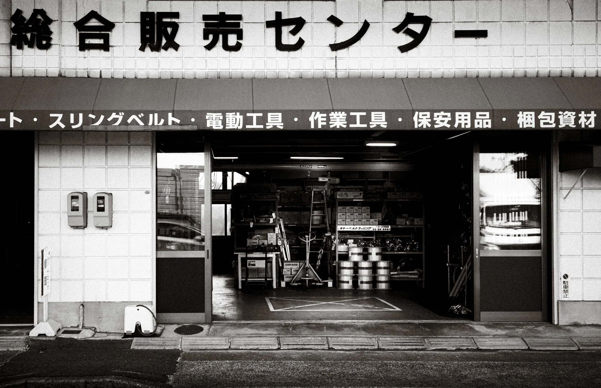 An open shop entrance reveals shelves and stacked containers beneath a broad lettered sign.