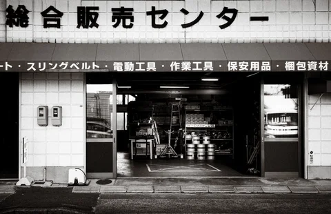 An open shop entrance reveals shelves and stacked containers beneath a broad lettered sign.