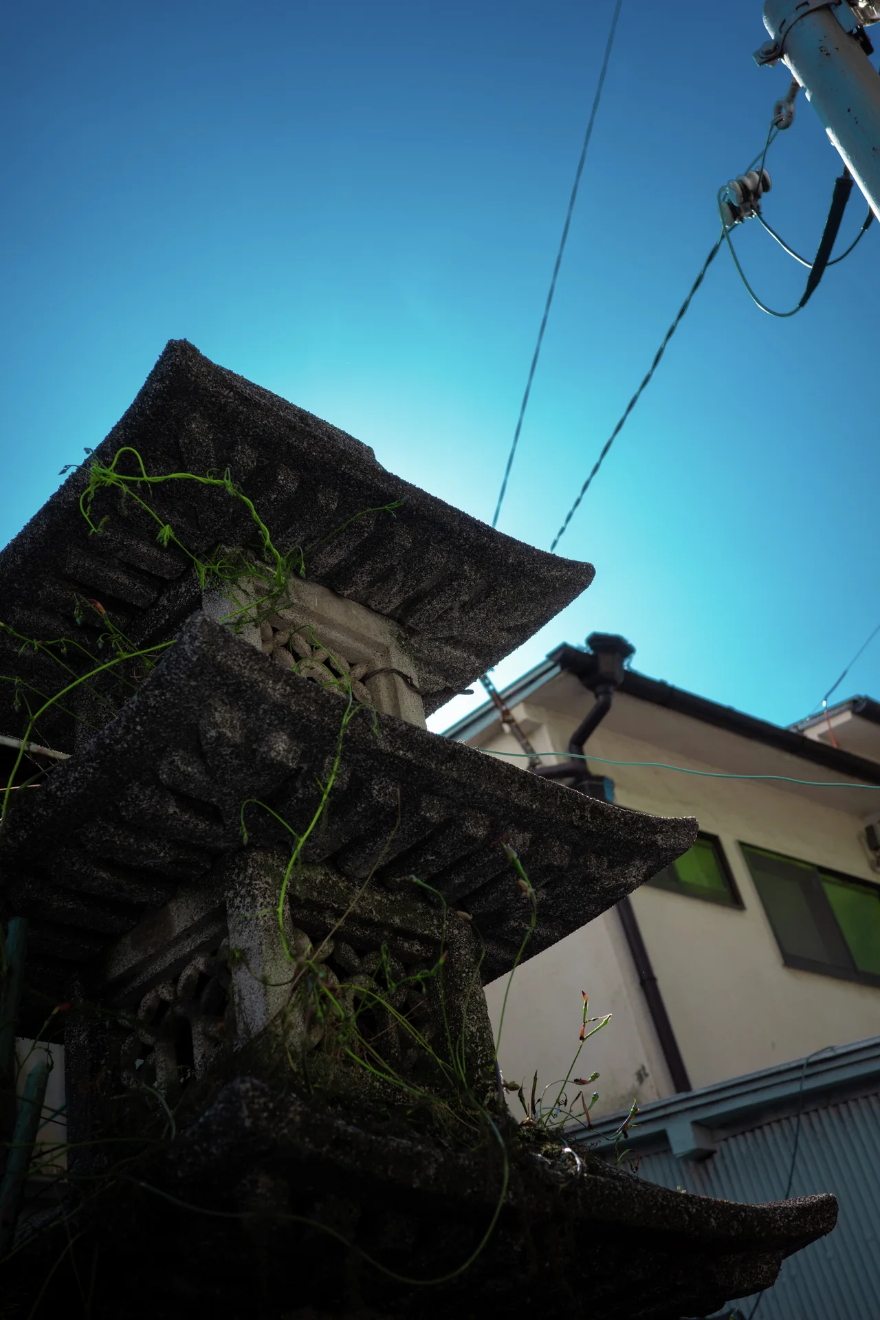 Layered tiled eaves rise sharply against a turquoise sky crossed by overhead utility wires.