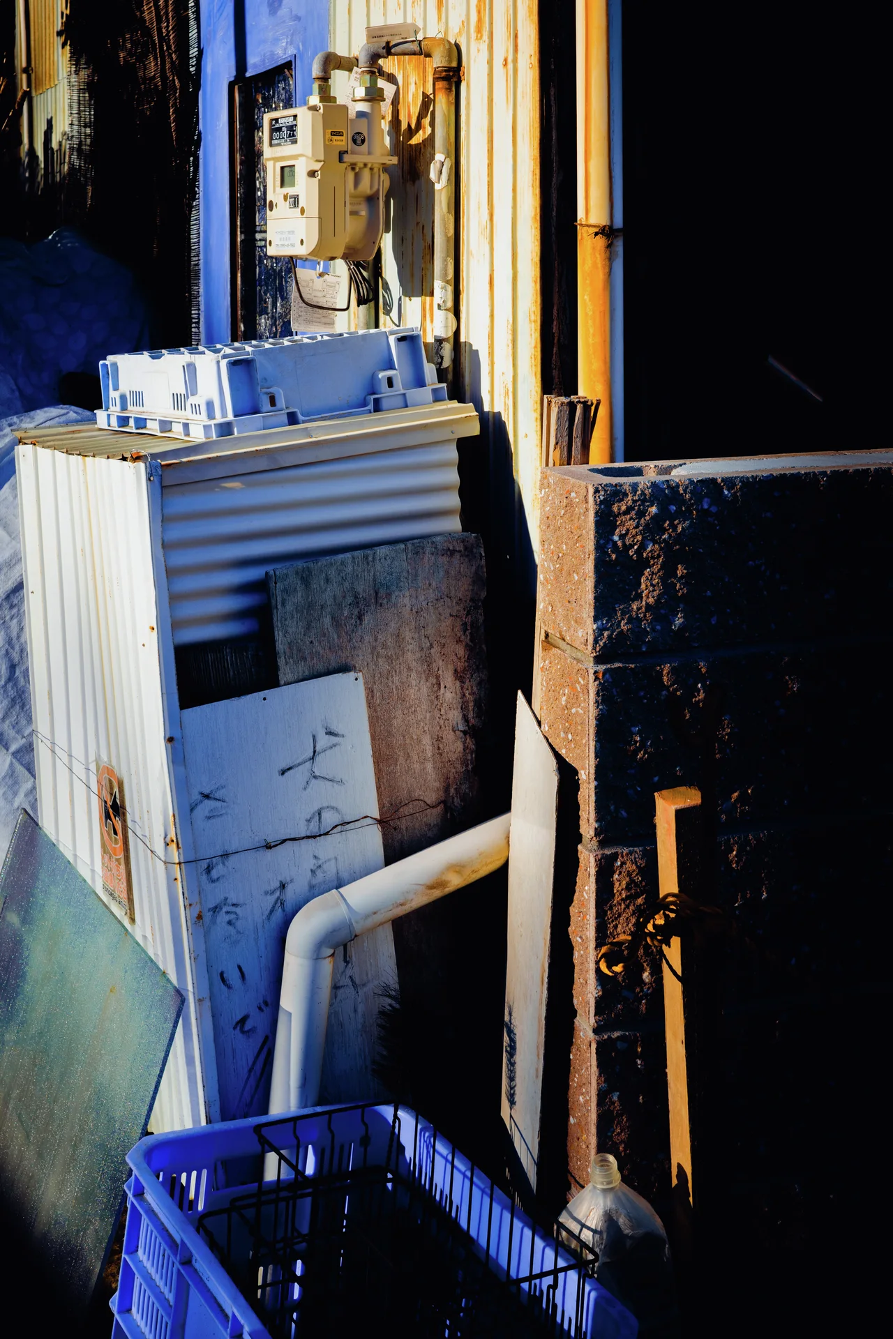 Small containers rest on weathered exterior equipment beside pipes and a blue plastic crate.