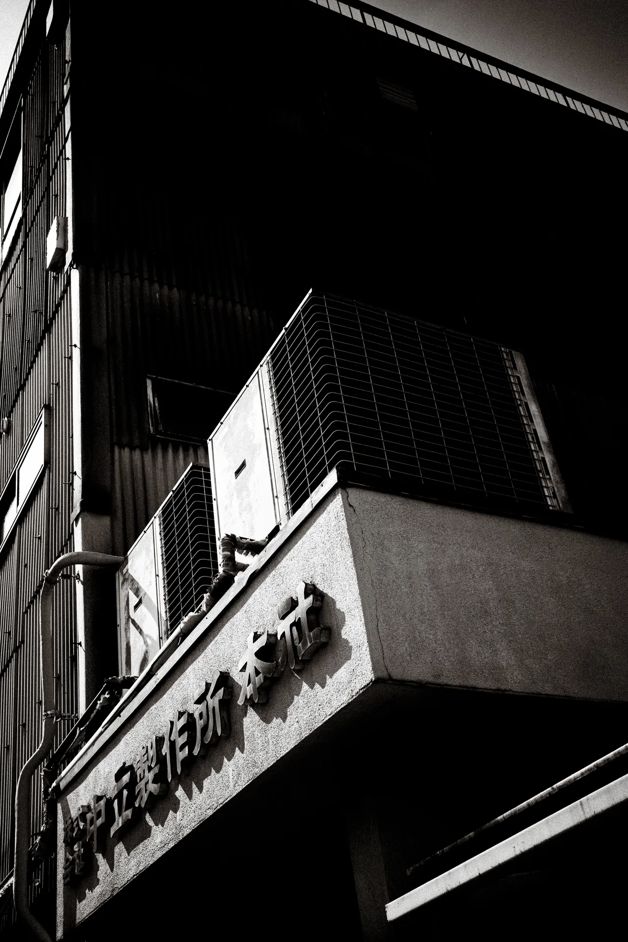 A large air conditioner rests on a projecting ledge above raised lettering in monochrome.