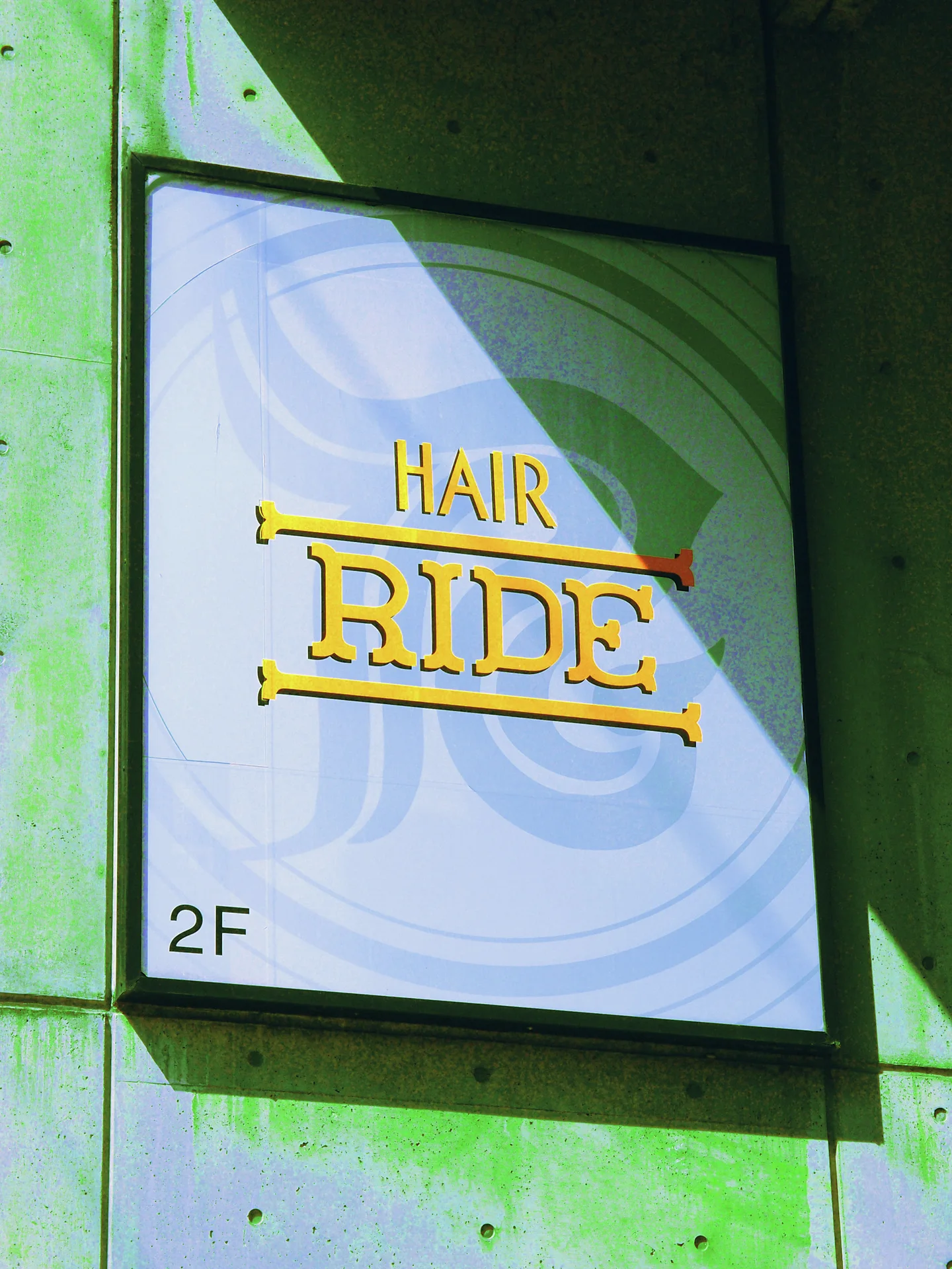 Gold HAIR RIDE lettering fills a framed pale sign on a green-stained concrete wall.
