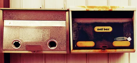 Two weathered metal mailboxes sit side by side, one with circular openings and one with yellow accents.