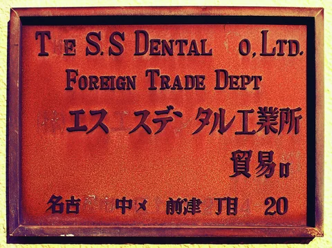 A framed reddish metal plaque bears English and Japanese lettering in dark raised characters.