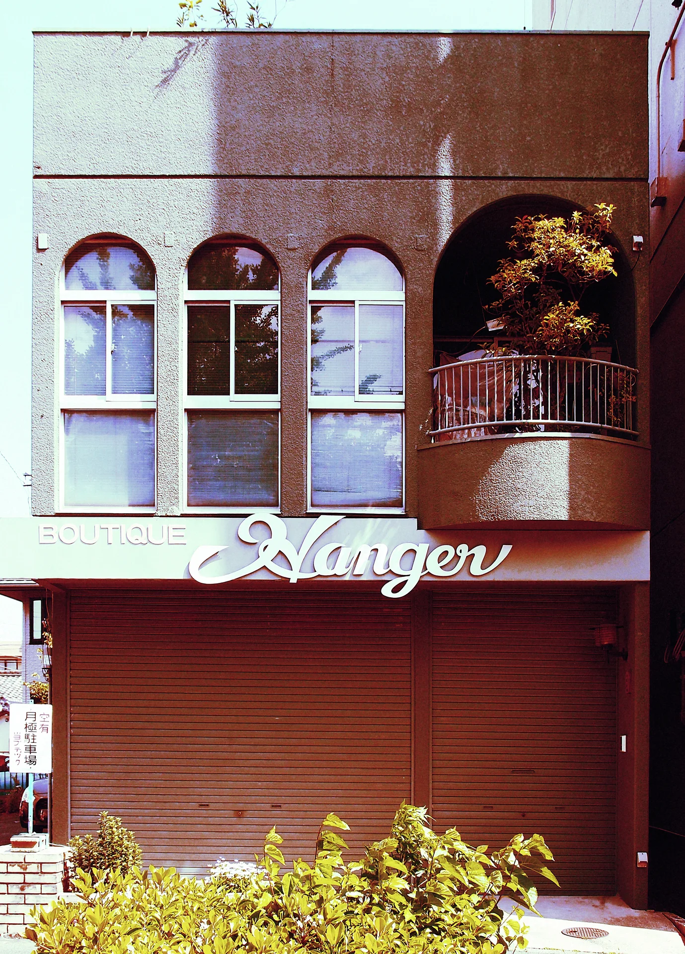 Three arched upper windows and a rounded balcony sit above a closed brown storefront shutter.