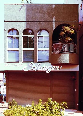 Three arched upper windows and a rounded balcony sit above a closed brown storefront shutter.