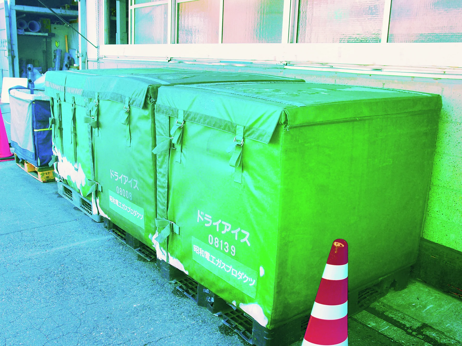Large green fabric-covered containers line a wall beside a pink and white traffic cone.