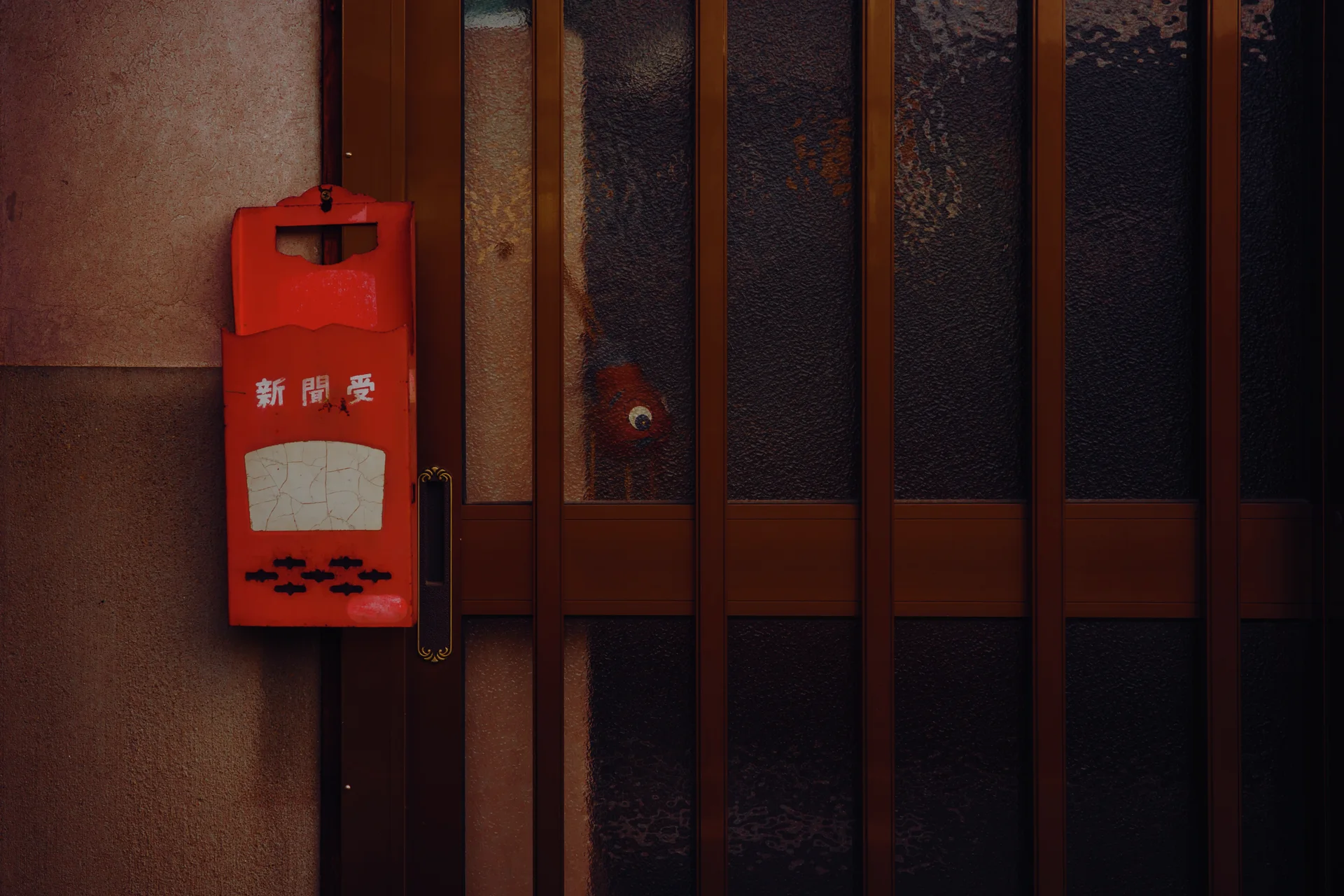 A red newspaper box hangs beside a dark wood-framed door with tall textured glass panels.