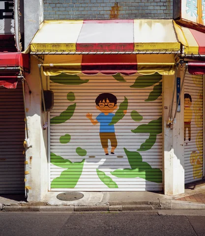 A cartoon child and green leaf shapes decorate a closed shop shutter beneath a striped awning.