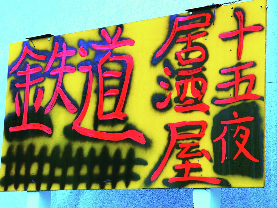 Bold red Japanese lettering with dark outlines fills a yellow sign mounted against turquoise walls.