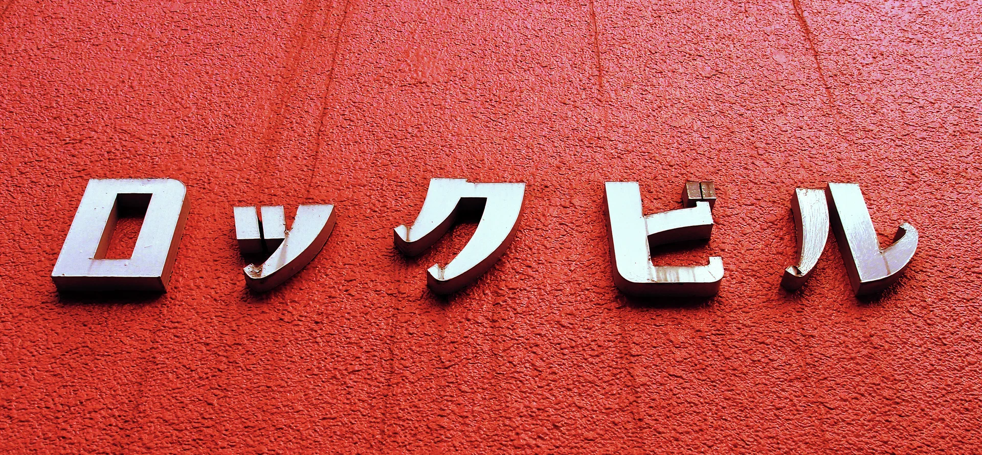Raised pale Japanese characters cast dark shadows across a textured reddish-orange wall.