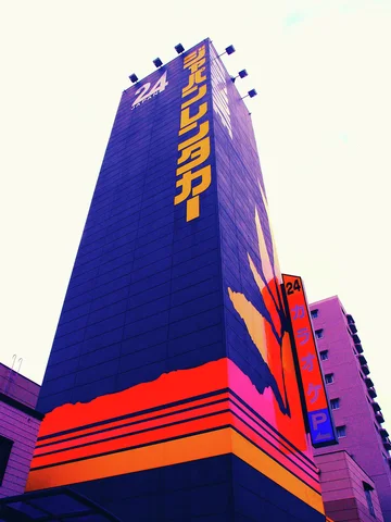 A tall purple sign tower has yellow vertical lettering and bright orange stripes near its base.